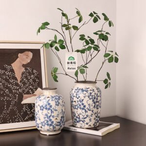 Two handcrafted blue and white floral ceramic vases sitting on a table next to framed wall art, with green botanical branches inside one vase