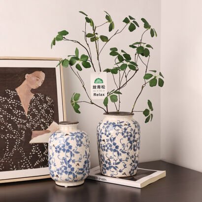 Two handcrafted blue and white floral ceramic vases sitting on a table next to framed wall art, with green botanical branches inside one vase