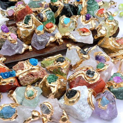 A colorful assortment of raw, unpolished crystal gemstone pendants featuring rough natural stones wrapped in textured gold electroplating and embedded with contrasting mini druzy and stone accents.