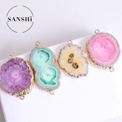 A row of four colorful natural solar agate geode slice pendants featuring purple, mint green, white and yellow, and pink crystals, each framed with raw textured gold electroplated edges and top/bottom connector loops against a white surface with a SANSHI brand logo.