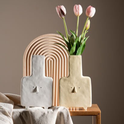 Minimalist ceramic square vases with abstract minimalist face features holding pink tulips on a wooden side table
