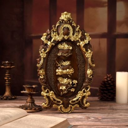 An ornate oval baroque-style wall plaque standing upright on a wooden table flanked by candlesticks and books, featuring a rich brown and metallic gold sculpted frame enclosing stacked sacred heart motifs with a crown of thorns and floral elements.