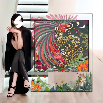 A large transparent acrylic art display frame resting on a light wood floor next to a modern staircase, featuring a central square silk scarf artwork of a spotted leopard with vibrant feathery plumage surrounded by lush tropical foliage and jungle wildlife.