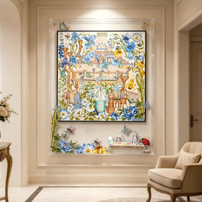 A large transparent acrylic display frame mounted on a cream entryway wall, featuring a central silk scarf illustration of a French perfumery mansion surrounded by blue floral blooms and copper distillation stills, accented with floating 3D-effect flowers, bees, butterflies, and perfume bottles on the clear outer frame border.