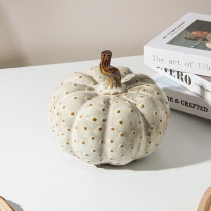 Cream ceramic pumpkin decoration with raised polka dot texture and brown twisted stem on a tabletop