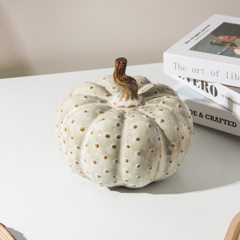 Cream ceramic pumpkin decoration with raised polka dot texture and brown twisted stem on a tabletop