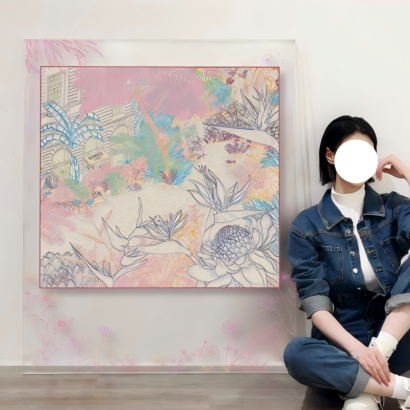 A large transparent acrylic framed artwork displayed next to a person sitting on the floor, featuring a central square silk scarf design of pastel tropical flora and architecture, with soft pink floral branch illustrations extended onto the clear outer border.