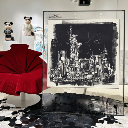 A large transparent acrylic art frame resting on the floor in a modern room near a red accent chair, displaying a monochromatic black and white silk scarf artwork of the Statue of Liberty and New York City skyline.