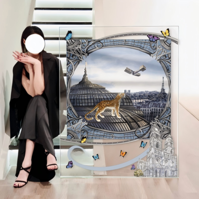 A large transparent acrylic art display placed on the floor next to a person sitting on stairs, featuring a framed silk scarf artwork depicting a leopard standing on the domed roof of the Grand Palais in Paris with flying butterflies and architectural accents.