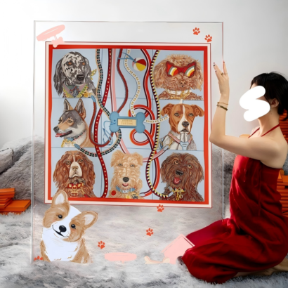 A large transparent acrylic art display held by a person in a red dress, featuring a framed silk scarf with detailed portraits of various dog breeds, colorful leashes, and cute paw print accents.
