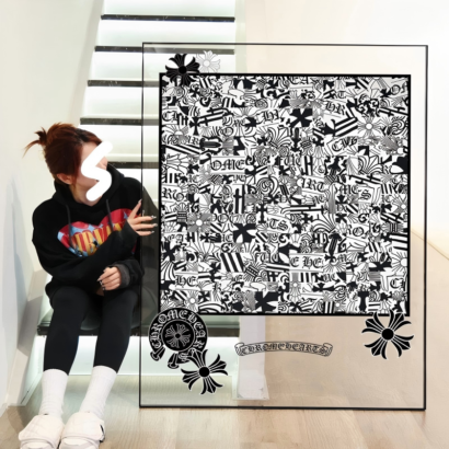 A large transparent acrylic art frame resting on the floor next to a person sitting on stairs, featuring a dense black and white gothic pattern collage surrounded by gothic cross motifs.