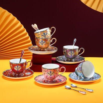 An assortment of colorful ceramic teacups and saucers with matching spoons displayed against a dark background with yellow paper fans, featuring intricate traditional Chinese cloisonné enamel patterns in red, yellow, pink, blue, and black.