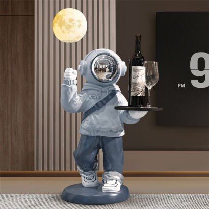 Modern floor-standing astronaut statue in a light blue hoodie holding an illuminated glowing moon lamp balloon and a tray with a wine bottle and glass