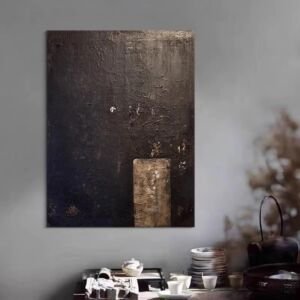 A vertical large dark textured canvas art piece mounted on a muted grey wall above a traditional tea table arrangement, featuring a heavily distressed charcoal black surface with a contrasting metallic bronze textured rectangle block at the lower right.