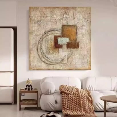 A modern minimalist living room featuring a large square textured canvas wall art mounted on a cream wall above a white sofa, showcasing overlapping geometric rectangular blocks and carved concentric circular lines in warm earth tones and sage green.