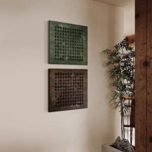 A warm minimalist interior scene featuring a vertical set of two square textured canvas artworks mounted on a beige wall, one in deep forest green and the other in dark earthy brown, each displaying a geometric grid pattern of 3D relief teardrop motifs.