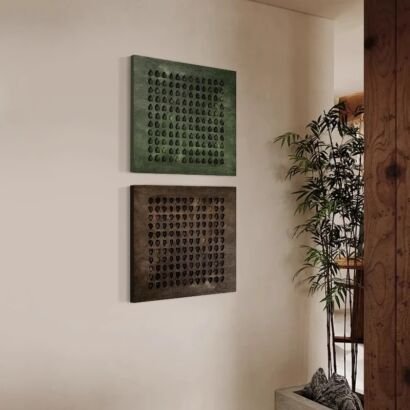 A warm minimalist interior scene featuring a vertical set of two square textured canvas artworks mounted on a beige wall, one in deep forest green and the other in dark earthy brown, each displaying a geometric grid pattern of 3D relief teardrop motifs.