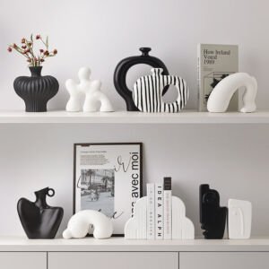 Collection of modern abstract black and white ceramic vases, hollow donut vessels, arch sculptures, and bookends arranged on minimalist white display shelves