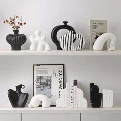 Collection of modern abstract black and white ceramic vases, hollow donut vessels, arch sculptures, and bookends arranged on minimalist white display shelves
