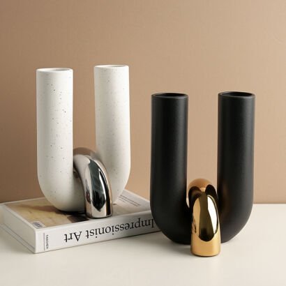 Pair of modern U-shaped ceramic vases in white terrazzo with silver chrome and matte black with gold chrome interlocking loops resting on a tabletop
