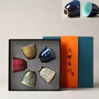 A luxury gift box containing five small ceramic teacups in various kiln-transformed glaze colors including deep blue, magenta pink, celadon green, beige crackle, and metallic grey.