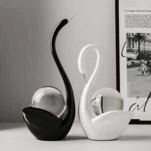 Pair of sleek black and white swan sculptures with metallic silver beaks cradling clear crystal spheres on a tabletop next to framed wall art