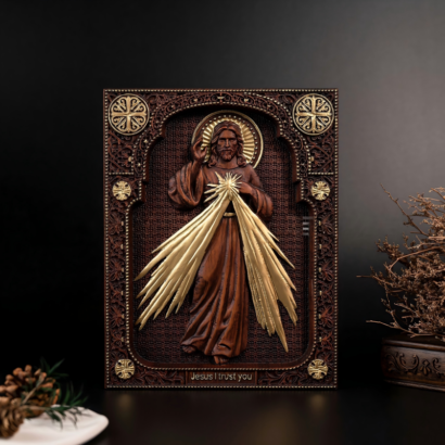 An upright rectangular wooden wall plaque featuring a detailed high-relief carving of Divine Mercy Jesus with glowing golden rays emanating from His chest and the inscription "Jesus I trust you", enclosed within an intricately carved and accented border, displayed on a dark surface next to pinecones.