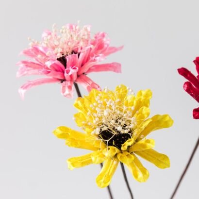 Close-up of bright pink and yellow artificial flowers with delicate white baby's breath center details against a plain light gray background
