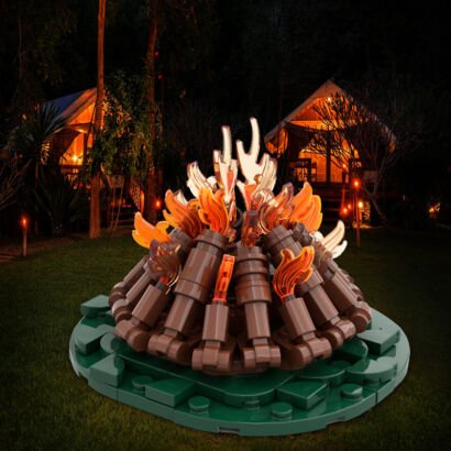 A LEGO-style building block model of a cozy outdoor campfire featuring brown log bricks and translucent orange and clear flame pieces set on a green base, displayed against a nighttime campsite background with glowing tents.