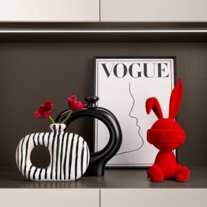 Black and white vertical striped donut ceramic vase with red flowers, solid black hollow vase, framed line art poster, and a velvet red rabbit figurine on a shelf