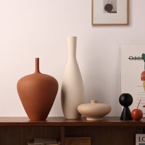 Assorted minimalist clay and ceramic vases in rust terracotta orange, off-white, and beige arranged on a dark wood cabinet