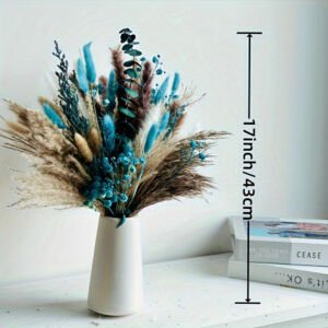 A 17-inch (43 cm) tall dried floral arrangement featuring neutral beige pampas grass, brown reed plumes, blue baby's breath, blue bunny tails, and dark green eucalyptus branches displayed in a white vase on a table with books.