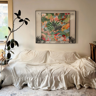 A large square transparent acrylic floating frame displaying a fine silk scarf with a zebra in a colorful tropical jungle, mounted above a sofa.