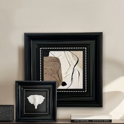 Set of two layered black square picture frames with white dotted trim, abstract textured painting and 3D white elephant relief artwork, displayed on dark wooden console table