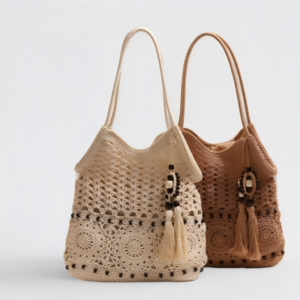 Two handwoven crochet straw shoulder tote bags in beige and tan sitting side-by-side against a plain white background, featuring circular floral motifs, dark bead accents, long shoulder straps, and hanging tassel bag charms.
