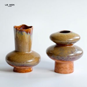 Two glossy olive green and warm amber terracotta glazed ceramic vases with abstract geometric silhouettes on a white surface