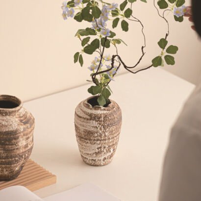 Rough brown and white textured ceramic stoneware vase holding delicate flowering branches on a tabletop