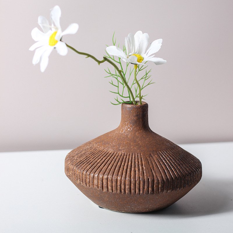 Earthy brown ceramic bud vase with fluted ribbed texture holding two white daisy blossoms on a table