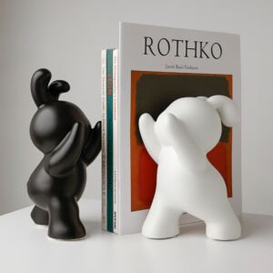 Pair of black and white cartoon bunny bookends in dynamic pushing poses holding up a stack of art books on a white table
