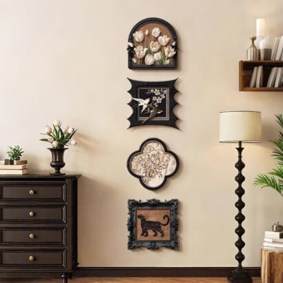 A vertical gallery set of four uniquely shaped black framed wall art pieces—including 3D white tulips, birds on blossom branches, vintage floral pattern, and a black panther—hung in a vertical line in a warm living room.