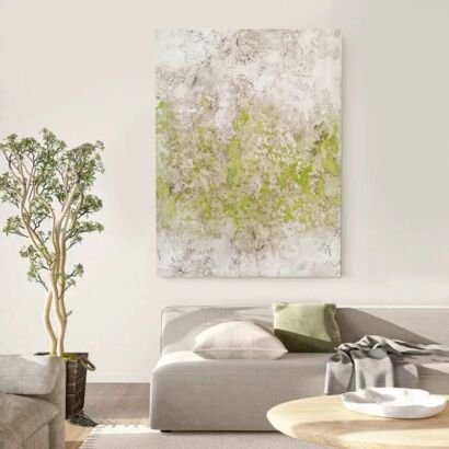 A vertical textured abstract canvas painting with subtle lime and moss green accents layered over a plaster-like beige background hanging above a modern couch in a neutral living room
