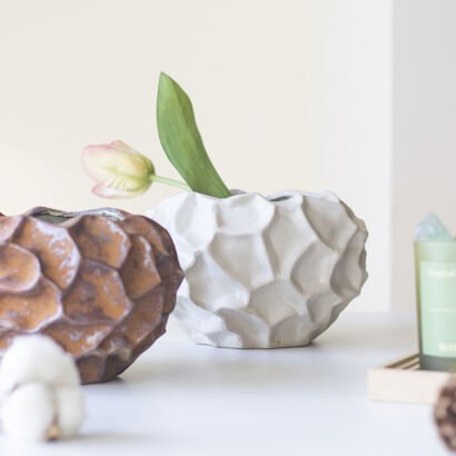 Off-white ceramic flower vase with a faceted honeycomb texture holding a single tulip stem on a bright desk