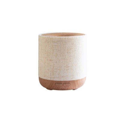 An isolated studio product shot of a compact cylindrical essential oil diffuser featuring a beige woven fabric cover, wood grain top and base, and minimal control buttons against a clean white background.