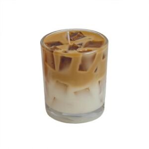 An isolated studio product shot of a realistic iced coffee scented soy candle in a clear glass tumbler, featuring layered white milk wax, espresso-colored swirl, wax ice cubes, and a single cotton wick on a plain white background.