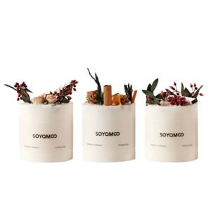 A trio of minimalist off-white soy scented candles decorated with dried botanical toppings including red berries, pinecones, cinnamon sticks, and green leaves.