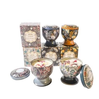 A collection of vintage floral patterned metal tin scented candles on pedestal bases, shown open with real dried flower petals alongside matching decorative packaging boxes.