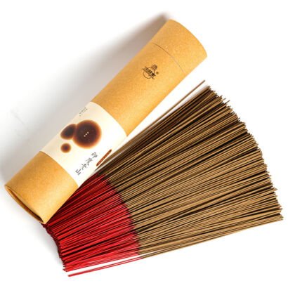 A fan of natural sandalwood incense sticks with red-dipped bamboo ends laid out beside an eco-friendly round kraft paper packaging tube.