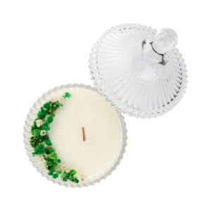 Top view of an open clear embossed glass candle jar filled with soy wax decorated with green and white dried flowers.