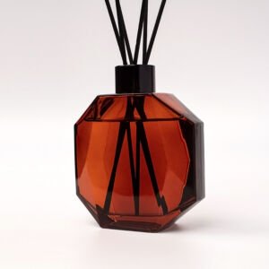 Faceted amber glass diffuser bottle with fanned black reeds on a white background.