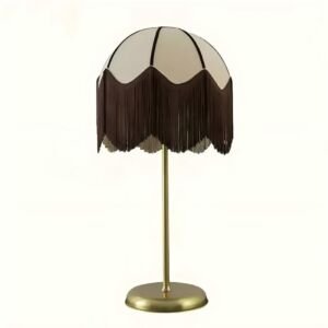 A vintage-style table lamp featuring a cream dome shade adorned with dark brown scalloped tassel fringe and dark piping trim, supported by a slim brass metal stand and round base isolated on a white background.